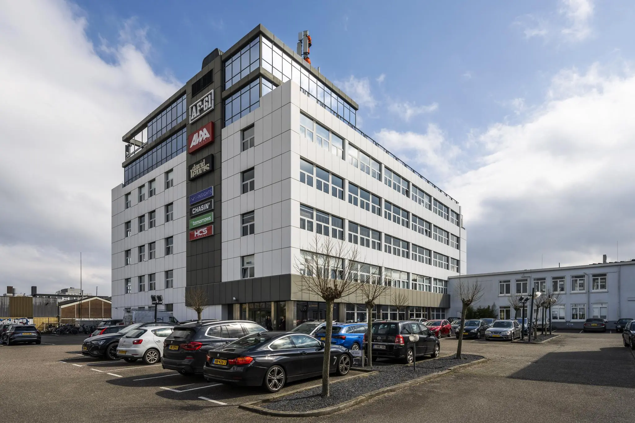 Kantoorgebouw aan de Anthony Fokkerweg met meerdere bedrijfslogo’s en een parkeerplaats op de voorgrond.